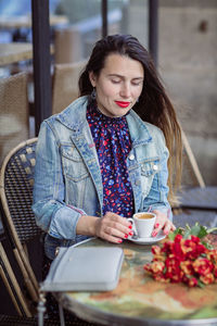 Attractive woman with long brunette hair in blue dress sitting in street cafe