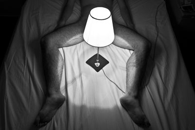 Low section of naked man lying with illuminated lamp on bed