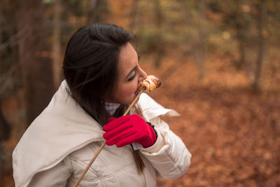 Close-up of young woman eating roasted marshmallow in forest