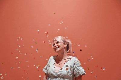 Smiling woman standing amidst confetti against wall