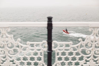 Jet boat in sea seen through palace pier railing on sunny day