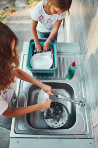 Teenager girl washing up the dishes pots and plates with help her younger sister in the kitchen