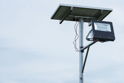 Low angle view of floodlight with solar panel on pole against clear sky