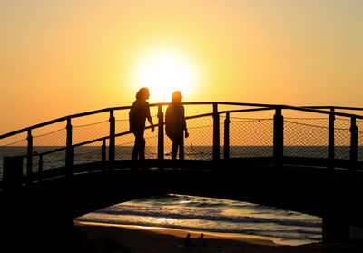 Silhouette people on railing against sea during sunset