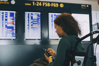 Side view of businesswoman using phone while sitting at airport