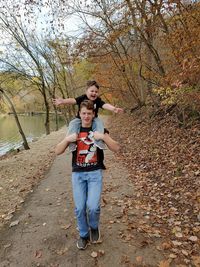 Full length portrait of boy standing on tree during autumn