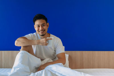 Portrait of a smiling young man sitting on bed