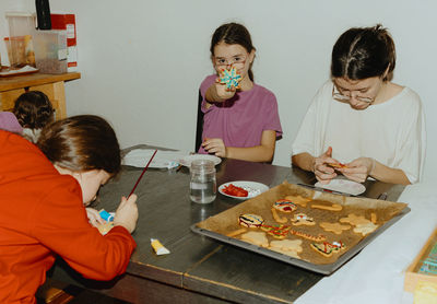 Three girls decorate cookies with fondant and chocolate while sitting at the table.