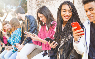 Friends using smart phones while sitting outdoors