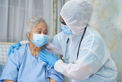 Doctor wearing hazmat suit consoling patient at hospital