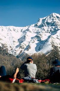 People sitting on snowcapped mountain against sky