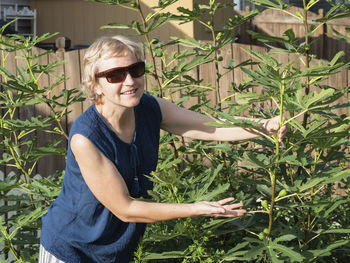 Mature woman wearing sunglasses standing by plants