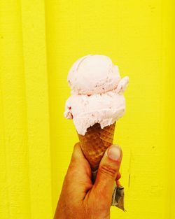 Cropped image of man holding ice cream cone against yellow wall