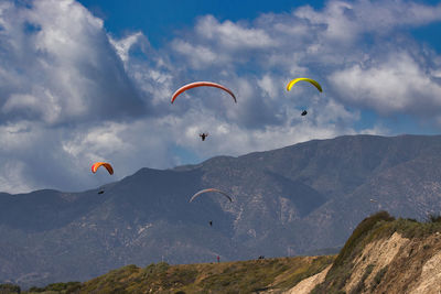 Low angle view of people paragliding against sky