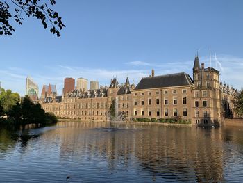 View of buildings by river against blue sky