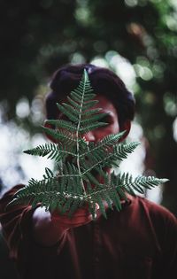 Close-up of boy holding leaves over face