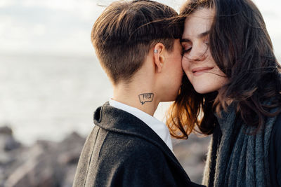 Lesbian women embracing while standing against sea