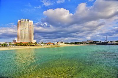 City buildings at waterfront against cloudy sky