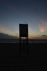 Lifeguard chair on beach against sky during sunset