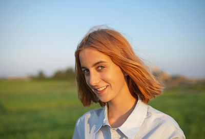 Smiling young woman standing on field against clear sky