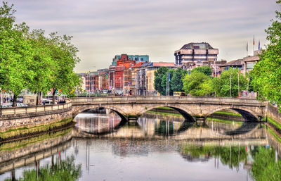 Arch bridge over river in city against sky