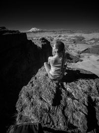 Woman sitting on cliff by mountain against sky