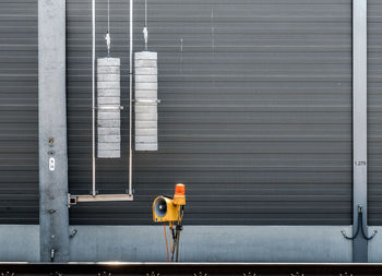 A railroad signal in front of a noise barrier, yellow in front of gray