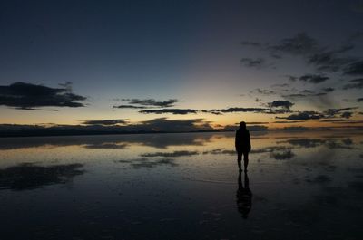 Silhouette of woman standing by lake at sunset