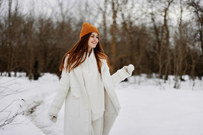 Smiling young woman standing on snow covered land