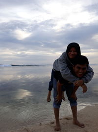 Man piggy backing girlfriend at beach against sky