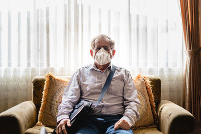 Senior man wearing mask sitting on sofa at home