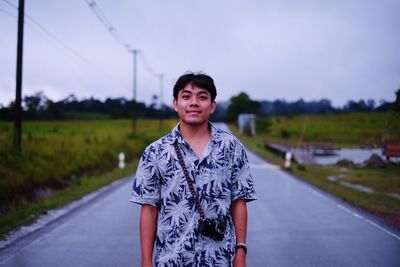 Portrait of smiling man standing on road against sky