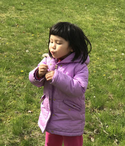 Girl blowing dandelion seeds while standing on field