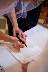 Close-up of bride signing on paper with groom on table