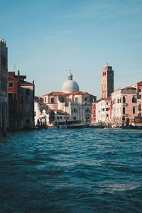 Canal amidst buildings against blue sky in city