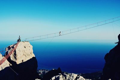 Mid distance view of person walking on rope bridge against blue sky