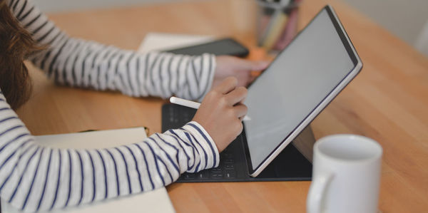 Midsection of woman using mobile phone while sitting on table