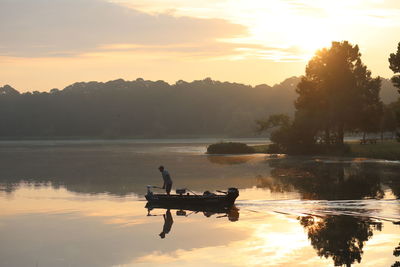 Silhouette boat in lake against sky during sunset