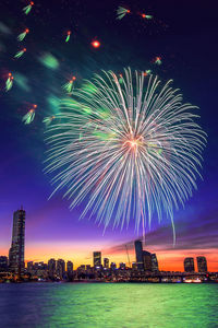 Low angle view of firework display over river in city