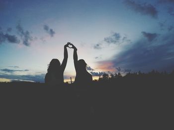 Silhouette friends making heart shape from hands against sky