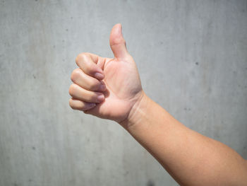 Cropped hand gesturing thumbs up against wall