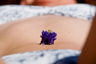 Purple flower on abdomen of woman lying outdoors