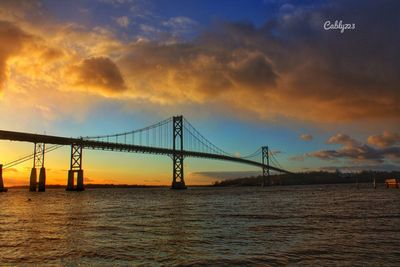 Suspension bridge over river against cloudy sky