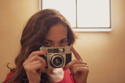 Portrait of woman photographing against yellow wall