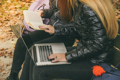 Girls study sitting on a bench in the park in a beautiful autumn afternoon. teens using laptop 