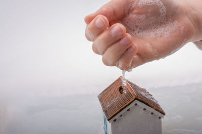 Close-up of hand washing model home against white background