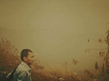 Side view of boy standing on field against sky