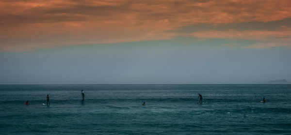 People in sea against sky at sunset