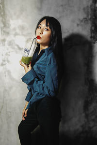 Side view of a young woman drinking glass against wall