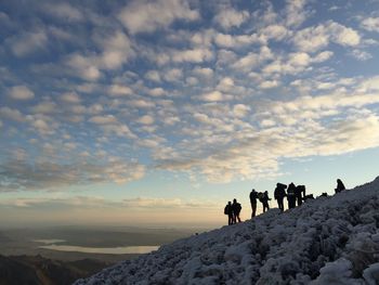 People standing on snow covered landscape against sky during sunset